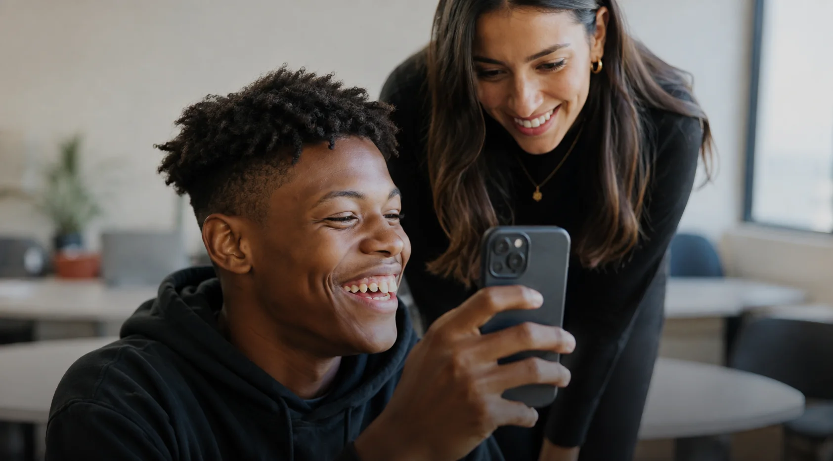 Profissional e estudante olhando juntos um celular em um ambiente de trabalho colaborativo.